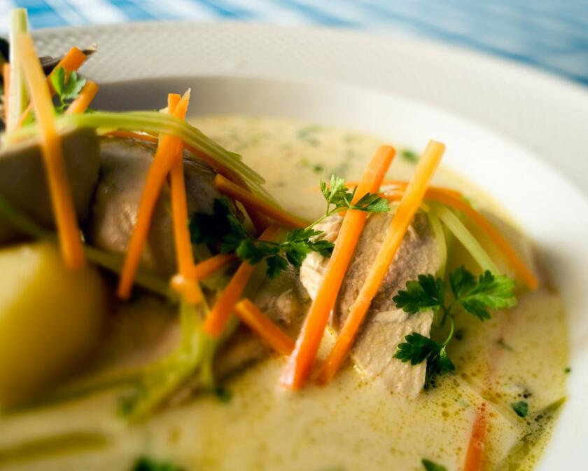 Une assiette de Gentse waterzooi : pommes de terre et poulet dans une assiette de soupe aux légumes. Vous voyez des carottes, du poireau et de l'oignon, le tout complété par du persil frisé.