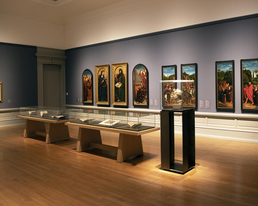 museumzaal met enkele taferelen van het lam gods, vitrinekasten 