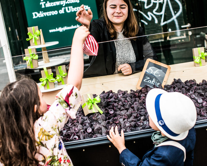 Verkoopster geeft een rood/wit gestreept zakje cuberdons aan twee kindjes aan het kraampje op de Groentenmarkt in Gent