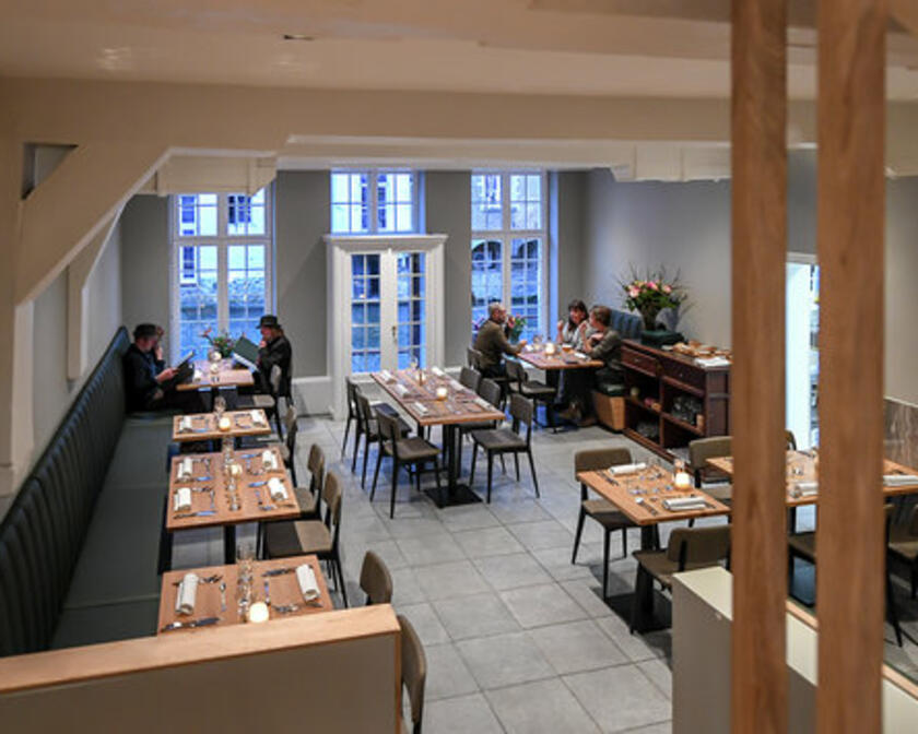Binnenzicht op het restaurant, grijze banken, natuurhouten tafels voor 2, 4 of meer.