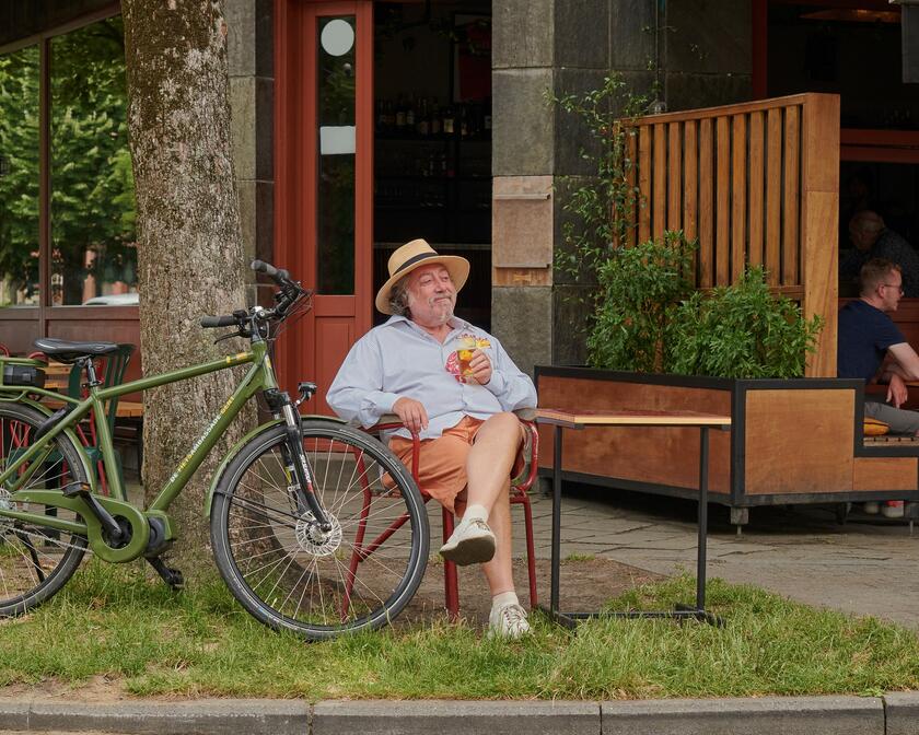 Man met hoed op die op het terras een drankje drinkt naast een donkergroene fiets