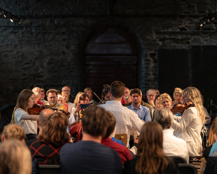 Scenes from Lauden 2023: an intimate string orchestra is surrounded by the audience present in the historic refectory of St Bavo's Abbey