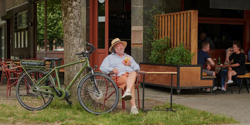 Man met hoed op die op het terras een drankje drinkt naast een donkergroene fiets