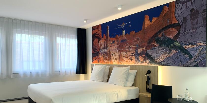 Room with double bed, wooden headboard and painting of Moebius 