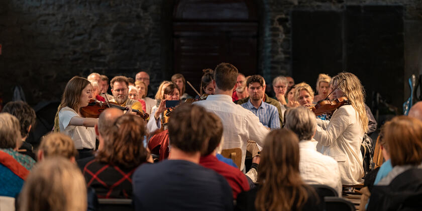 Scenes from Lauden 2023: an intimate string orchestra is surrounded by the audience present in the historic refectory of St Bavo's Abbey