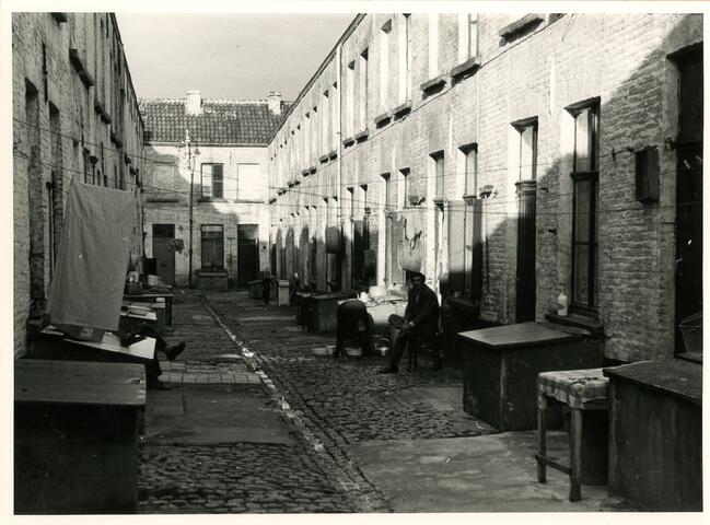Foto en blanco y negro de un residente sentado en una silla en un callejón de Gante