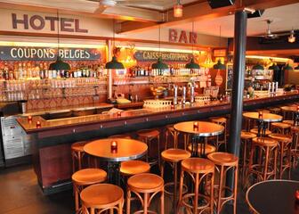 Leeg interieur van Bar des Amis met de bar zelf en hoge tafeltjes met barkrukken voor de toog.