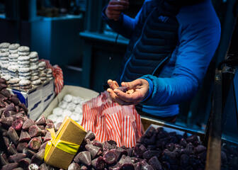 Verkäuferin mit blauem Pullover hält Cuberdons in der Hand und lehnt sich über einen Verkaufsstand mit Cuberdons und Schneebällen (typische Schokolade, rond und mit Puderzucker bestäubt). 