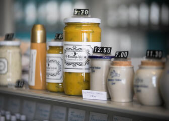 Different shapes, sizes and kinds of mustard lined up next to each other on top of a counter.