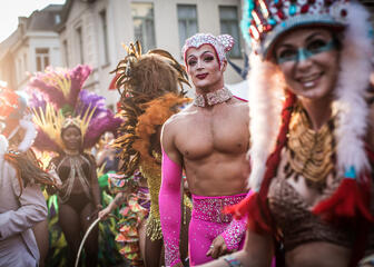 Mardi Gras parade tijdens de Gentse Feesten. Mensen in kleurrijke kostuums met focus op een man in een strak, felroze broek en handschoenen versierd met nepkristallen