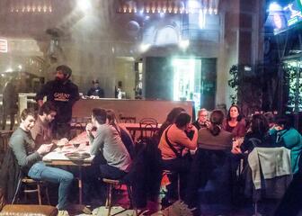 Mensen die in het Vooruit café aan tafels zitten, een lange bar met iemand achter.