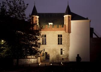 Poort Prinsenhof met bakstenen torentjes, 's avonds, verlicht.