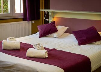 Tweepersoonsbed in een hotelkamer met paarse accenten.