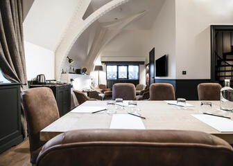 een ruimte met een lange houten tafel en bruine stoelen, bruine gordijnen aan het raam, zwarte accenten