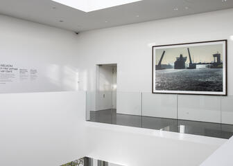 het startpunt in het STAM, witte ruimte met glazen balustrade, schilderij van de haven aan de muur