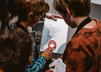 A group of children are looking at a New Year's letter. One of them uses a magnifying glass so you can see a stamp of a smiling face.