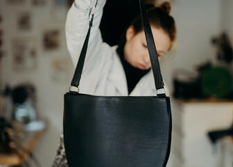 Die Designerin Griet Aesaert hält eine fertige halbmondförmige Handtasche in die Luft und prüft sie erneut.
