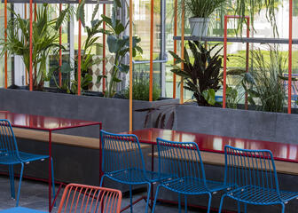Terraza con sillas y mesas metálicas en azul y rojo con varias plantas colgantes
