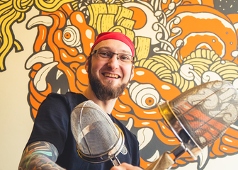 Chefkoch Nick posiert mit gekreuzten Abtropfsieben vor einem japanischen Wandgemälde im Hintergrund