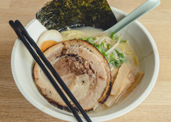 Bowl of ramen and slices of meat against a wooden background