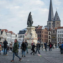 Gran plaza del Mercado del Viernes con estastua de Jacob van Artevelde, en el fondo la iglesia de Santiago, gente paseando.